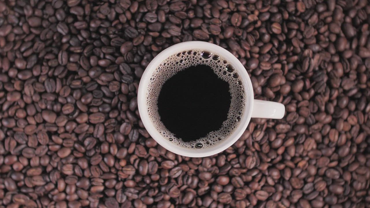 A cup of black coffee on a bed of roasted coffee beans