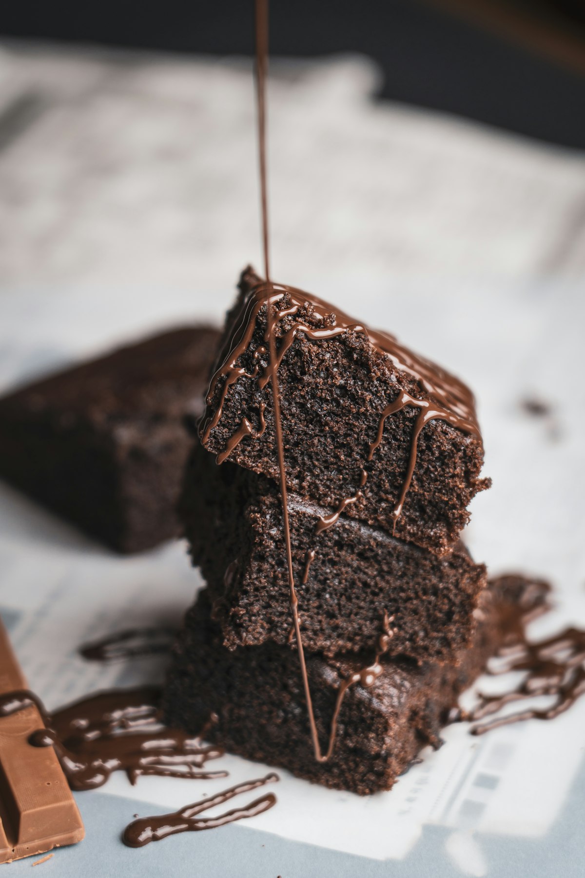 Stacked brownie slices with chocolate being poured over them